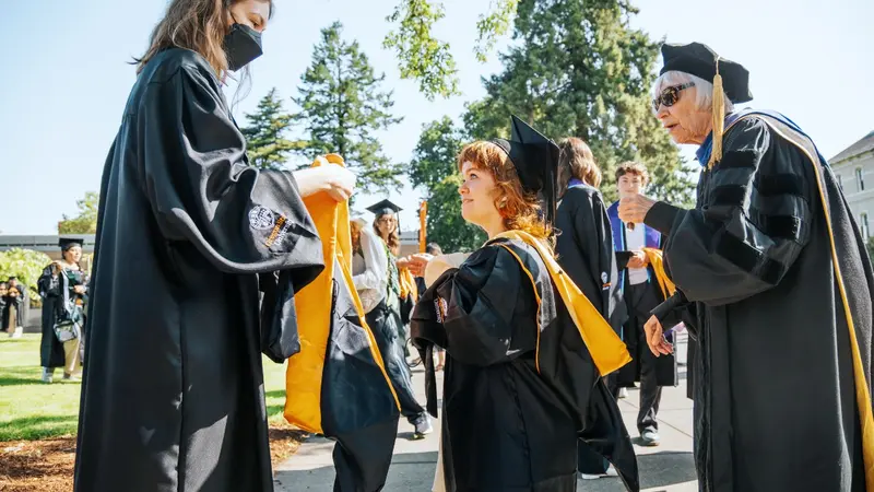 three masters students with their hoods at commencement